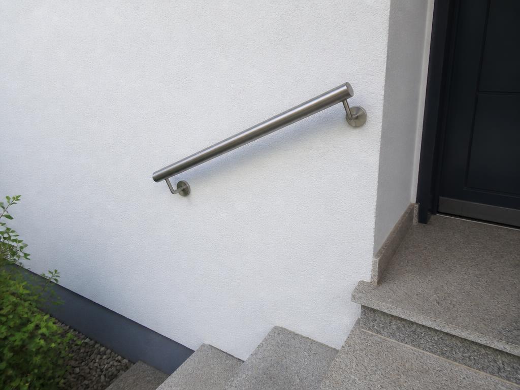 Kurzer Edelstahl-Handlauf an der Wand neben Stufen im Hauseingangsbereich